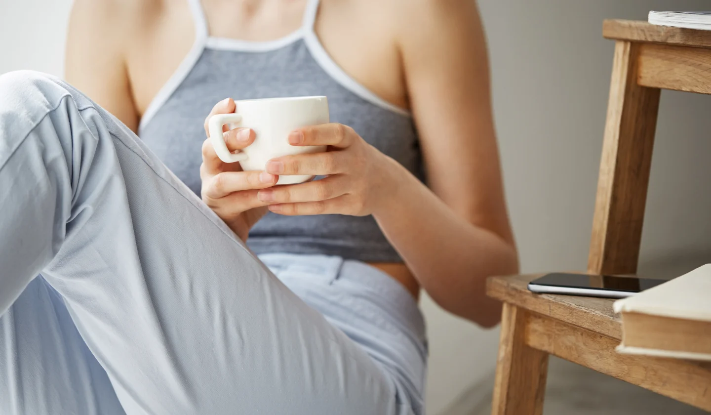 A woman sitting inside her home and relaxing, holding bowl of soup post surgery.