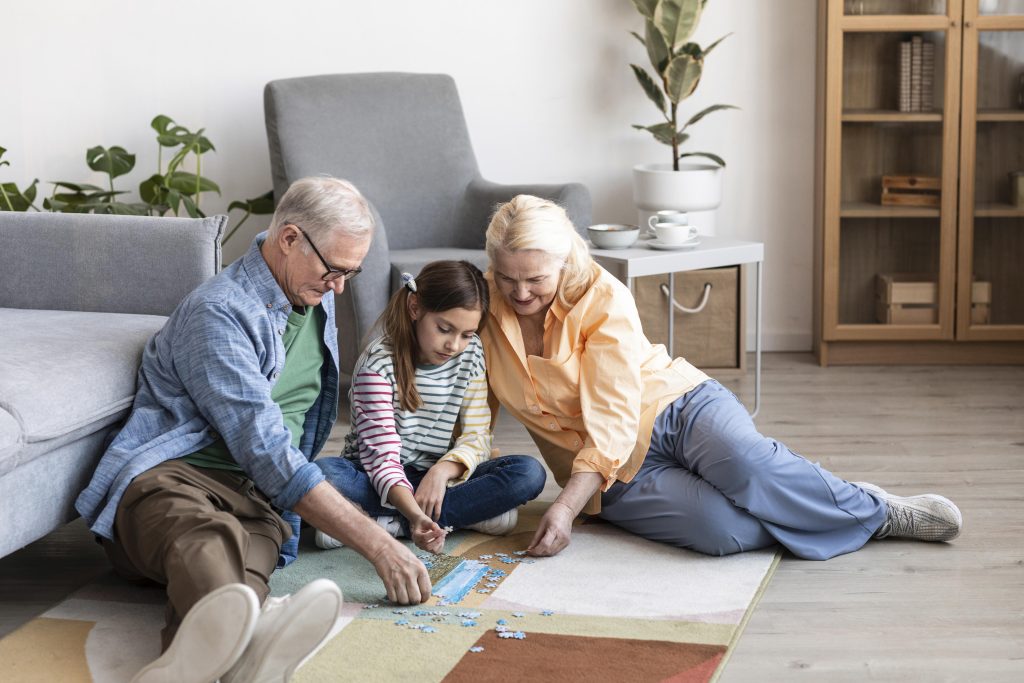 An elderly couple, fixing jigsaw puzzle pieces, comfortably sitting on the floor carpet with their granddaughter, and spending quality time as grandparents