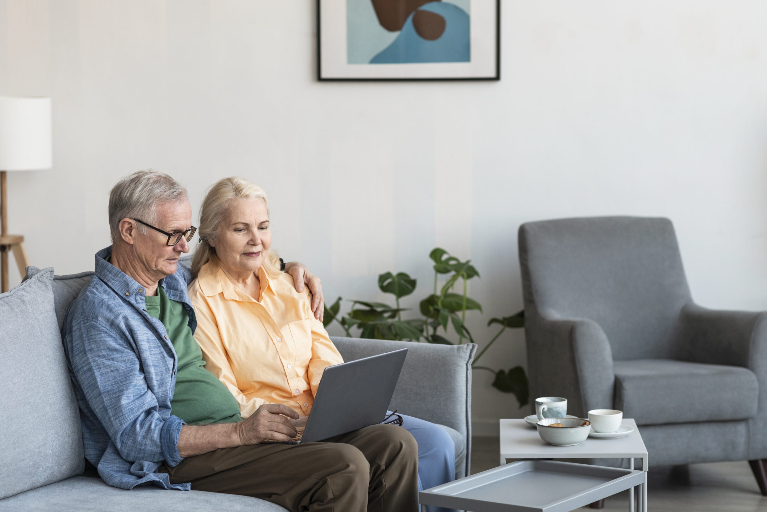 An elderly white couple sitting lovingly in their living room and receiving teleconsultation through their laptop screen as part of home health care in dubai